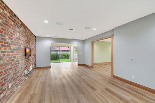 unfurnished living room featuring brick wall and light wood-type flooring