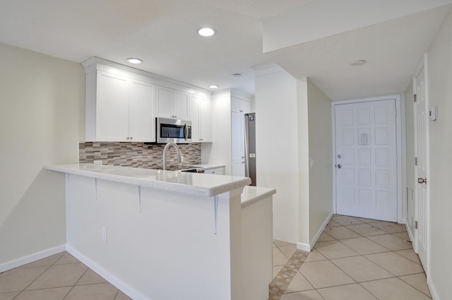 kitchen featuring white cabinets, kitchen peninsula, sink, light tile patterned flooring, and backsplash