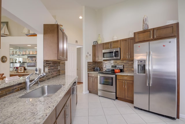 kitchen featuring light stone counters, sink, tasteful backsplash, light tile patterned floors, and appliances with stainless steel finishes