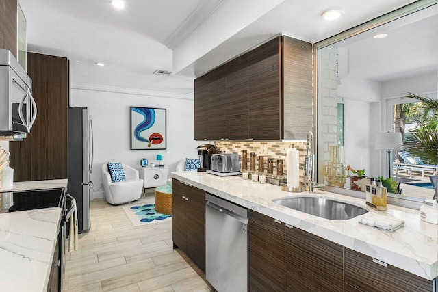 kitchen with light hardwood / wood-style floors, light stone countertops, ornamental molding, and appliances with stainless steel finishes