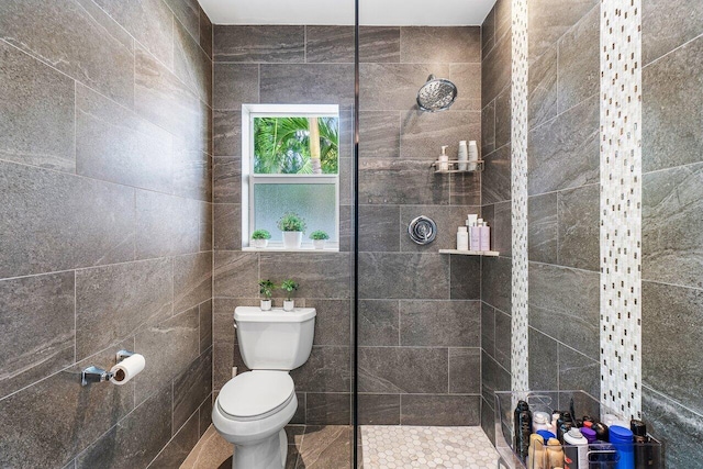 bathroom with toilet, a tile shower, and tile walls