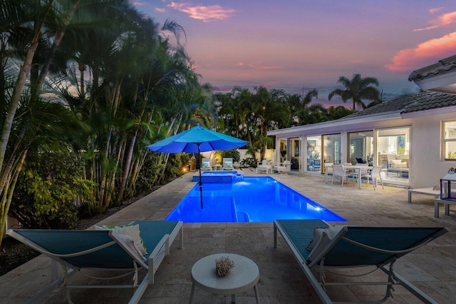 pool at dusk featuring an in ground hot tub and a patio area