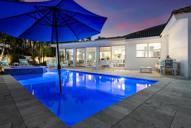 pool at dusk featuring an in ground hot tub and a patio