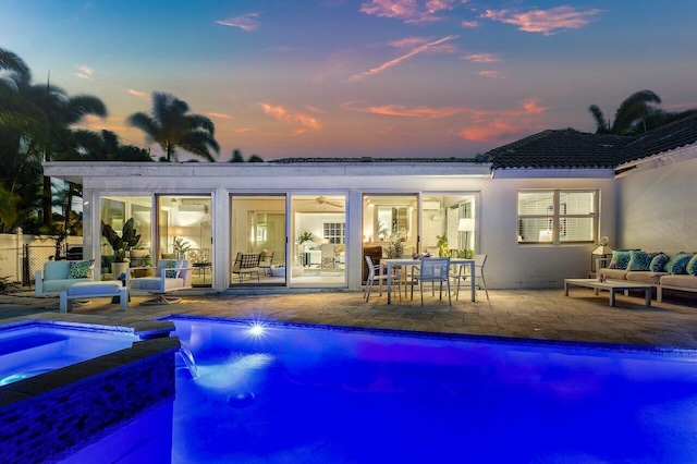 pool at dusk with outdoor lounge area, a patio area, and an in ground hot tub