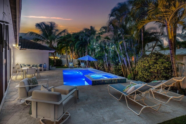 pool at dusk with an in ground hot tub and a patio area