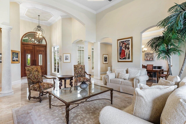 living room featuring a towering ceiling, a notable chandelier, crown molding, and decorative columns