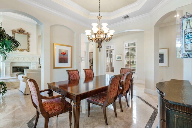 dining space with ornate columns, a raised ceiling, a chandelier, and crown molding