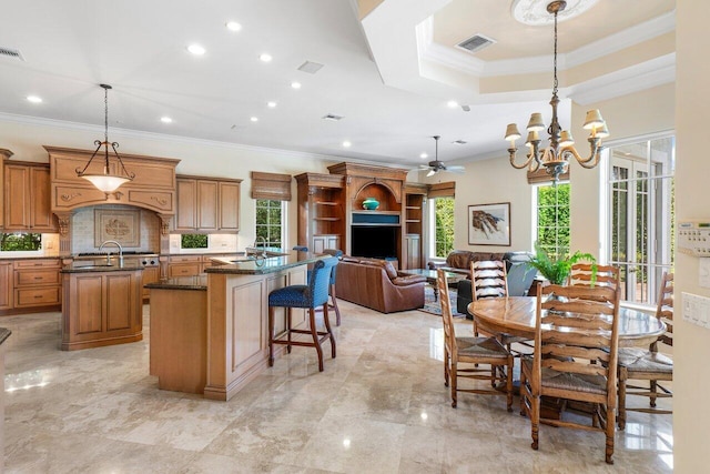 kitchen featuring a center island with sink, a breakfast bar, ornamental molding, ceiling fan with notable chandelier, and hanging light fixtures