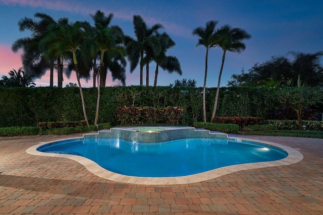 pool at dusk with a patio and an in ground hot tub