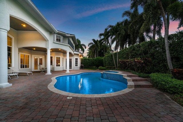 pool at dusk featuring an in ground hot tub and a patio area