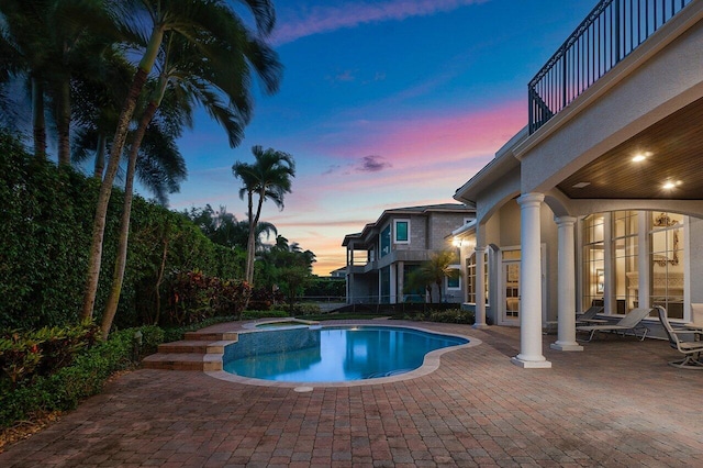 pool at dusk with a patio area and an in ground hot tub