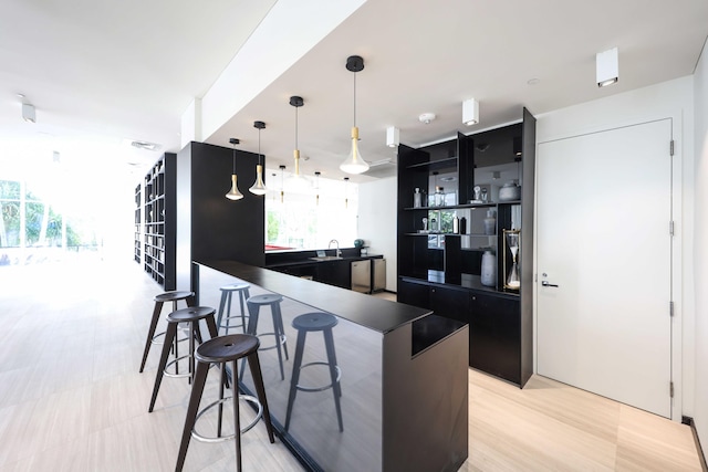 kitchen with decorative light fixtures, light wood-type flooring, sink, and a breakfast bar