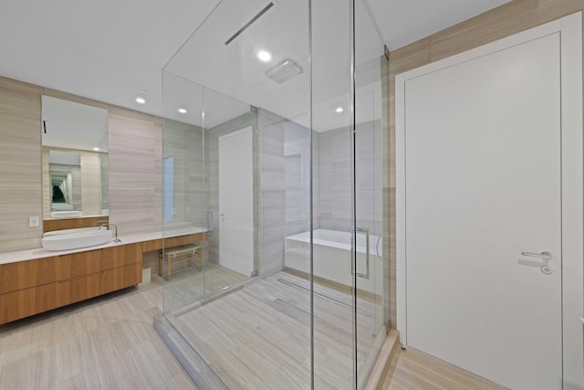 bathroom featuring plus walk in shower, vanity, and tile walls