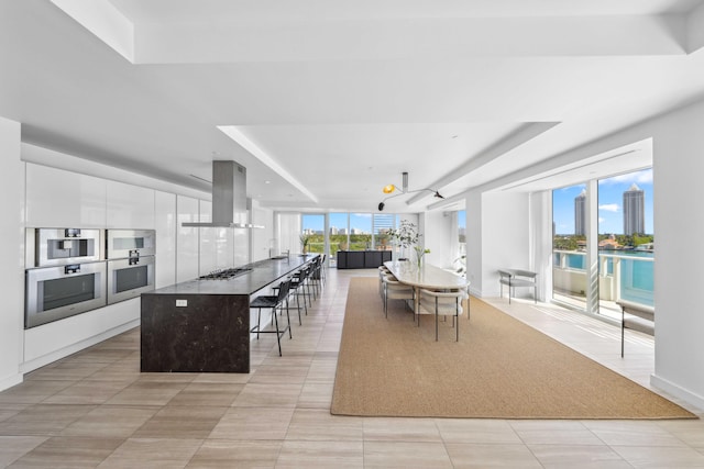 kitchen with a raised ceiling, island exhaust hood, white cabinetry, and a kitchen bar