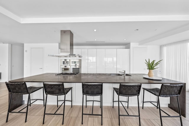 kitchen featuring island exhaust hood, a large island with sink, white cabinets, and a breakfast bar area