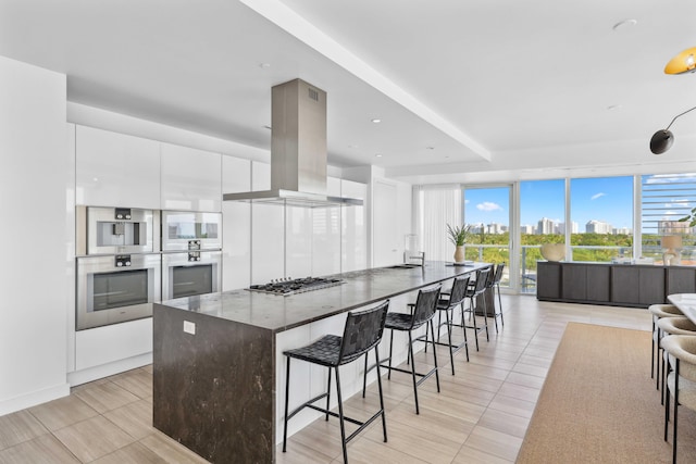 kitchen with a kitchen breakfast bar, dark stone countertops, island range hood, white cabinets, and appliances with stainless steel finishes