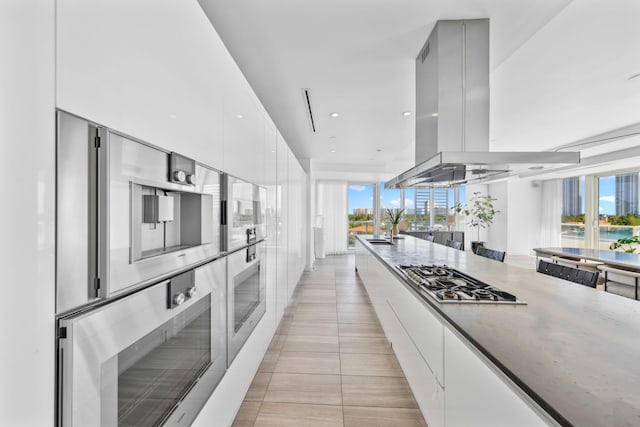 kitchen with light stone counters, island range hood, sink, white cabinetry, and stainless steel gas stovetop