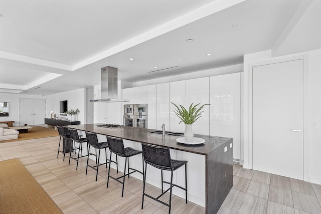 kitchen featuring white cabinetry, sink, a large island, wall chimney range hood, and a breakfast bar area