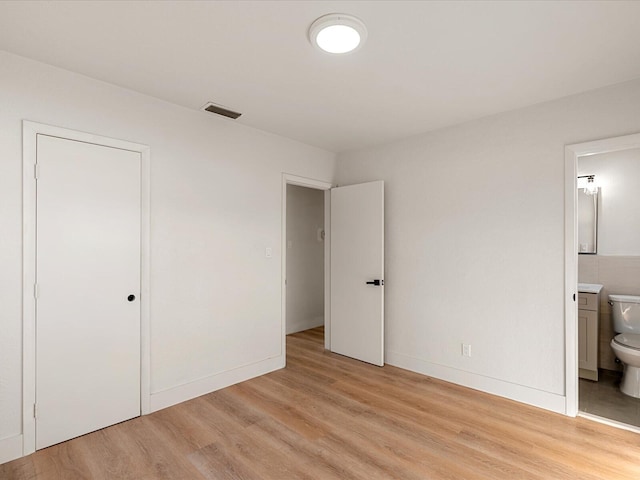 unfurnished bedroom featuring ensuite bath and light hardwood / wood-style flooring