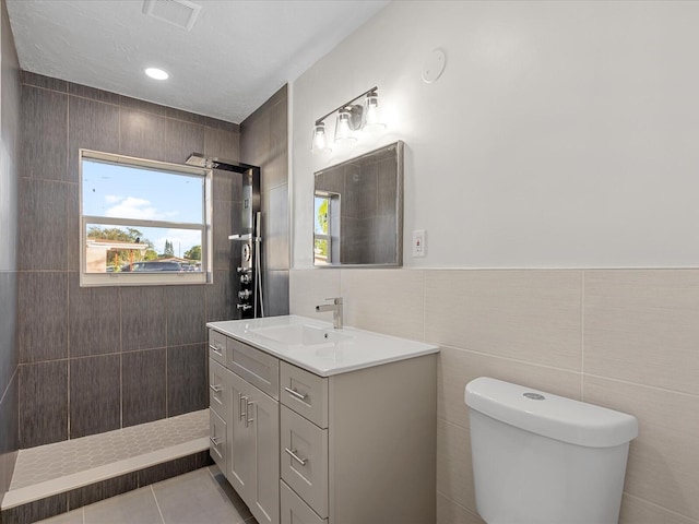 bathroom with vanity, tile patterned flooring, toilet, tiled shower, and tile walls