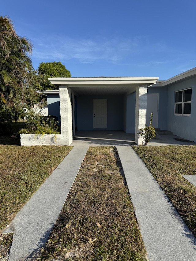 doorway to property with a lawn and a carport