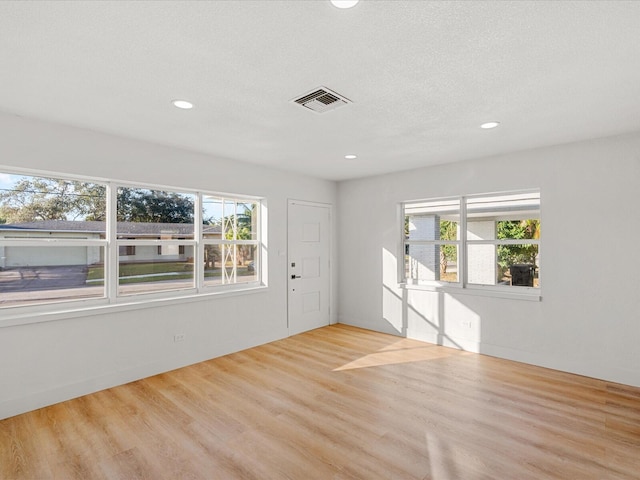 spare room featuring a textured ceiling, light hardwood / wood-style floors, and plenty of natural light