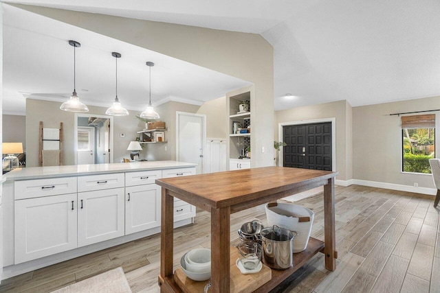 kitchen with lofted ceiling, crown molding, hanging light fixtures, light hardwood / wood-style flooring, and white cabinetry