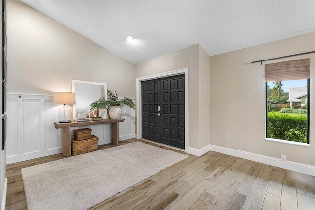 entrance foyer featuring light hardwood / wood-style floors, a textured ceiling, and vaulted ceiling