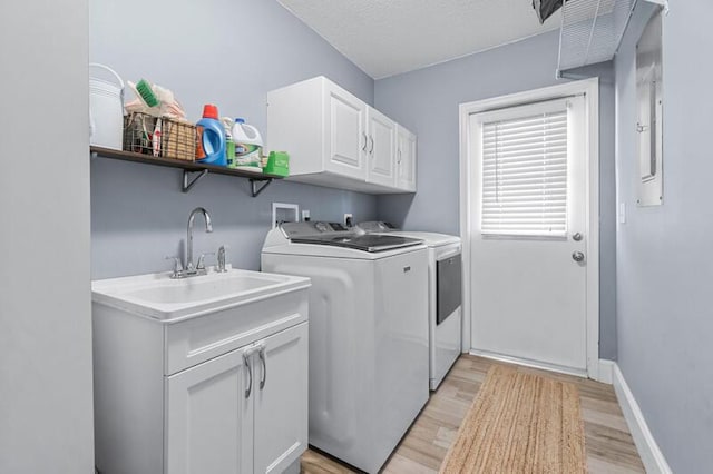 laundry room with cabinets, sink, a textured ceiling, light hardwood / wood-style floors, and washing machine and clothes dryer