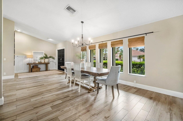 dining room featuring a textured ceiling, a notable chandelier, vaulted ceiling, and light wood-type flooring