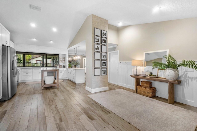 entryway with light hardwood / wood-style floors, a textured ceiling, high vaulted ceiling, and a chandelier