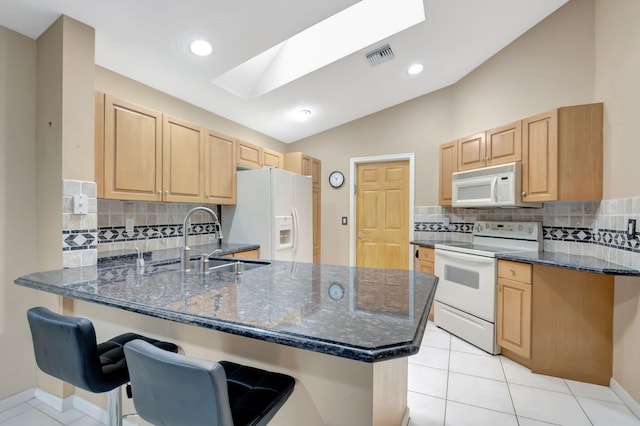 kitchen with a kitchen bar, kitchen peninsula, white appliances, dark stone countertops, and sink