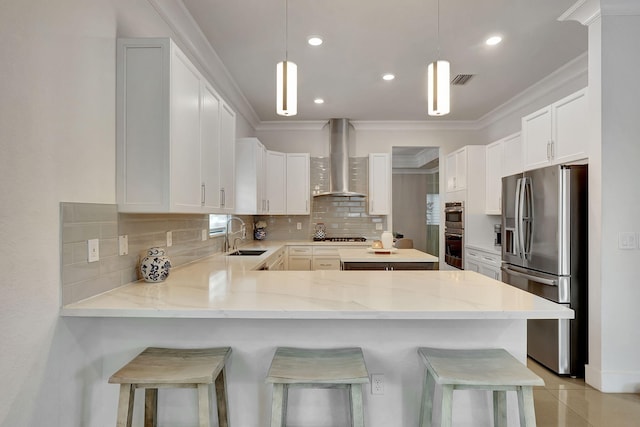 kitchen featuring wall chimney range hood, appliances with stainless steel finishes, hanging light fixtures, and a breakfast bar area