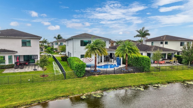 back of property with a water view, a patio, a yard, and a fenced in pool