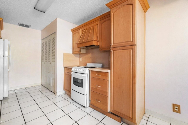 kitchen featuring a textured ceiling, light tile patterned floors, white appliances, and premium range hood