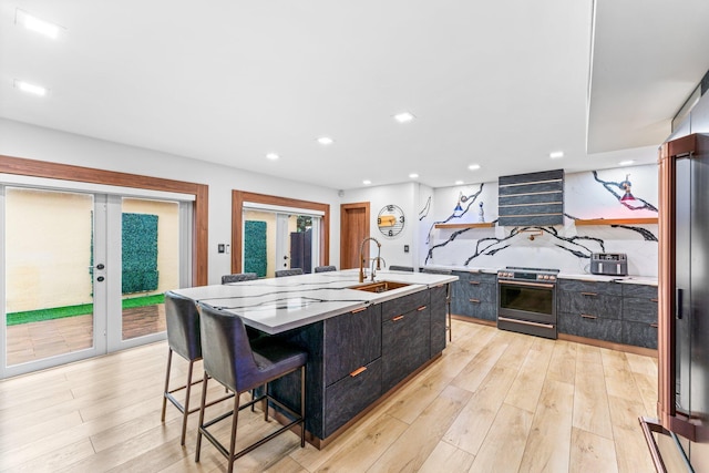 kitchen with a center island with sink, french doors, stainless steel range with electric cooktop, light wood-style floors, and a sink