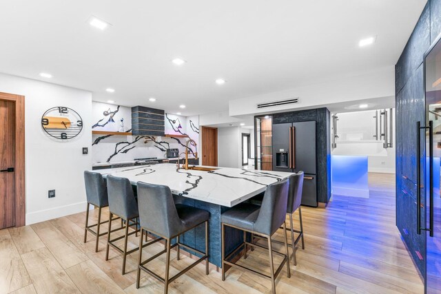 kitchen with light wood-style floors, recessed lighting, high quality fridge, and a kitchen bar