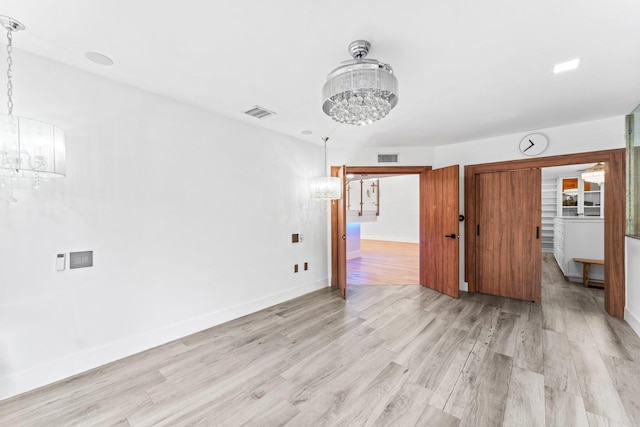 spare room featuring baseboards, light wood finished floors, visible vents, and a notable chandelier