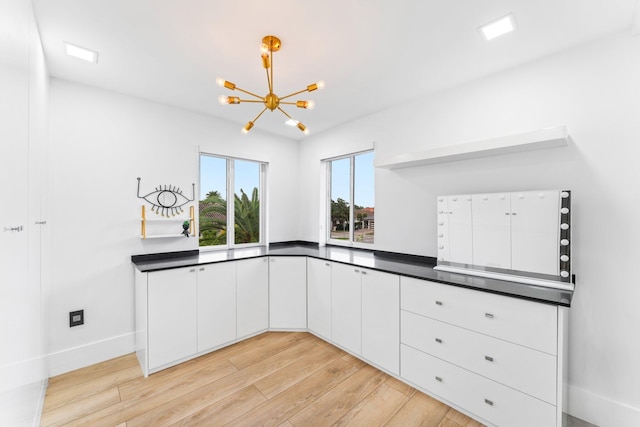 kitchen featuring dark countertops, an inviting chandelier, light wood-style flooring, and white cabinets