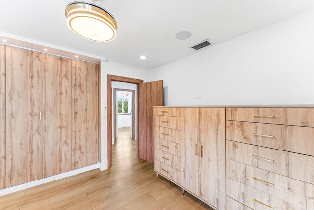 hallway with light wood-type flooring, visible vents, and baseboards