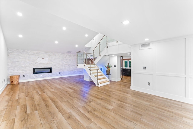 unfurnished living room featuring light wood finished floors, visible vents, stairs, a fireplace, and a decorative wall