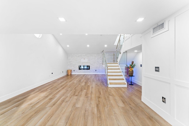 unfurnished living room with visible vents, baseboards, stairway, a stone fireplace, and light wood-style floors