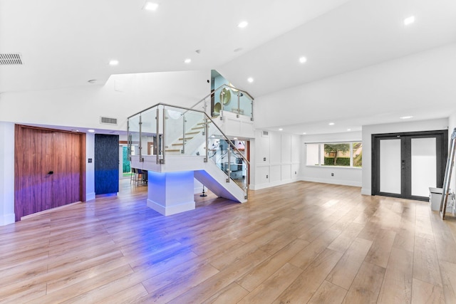 unfurnished living room featuring visible vents, stairway, french doors, light wood-type flooring, and high vaulted ceiling