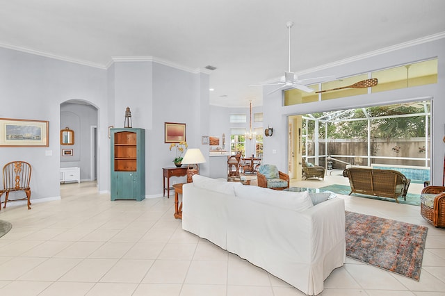 living room featuring arched walkways, crown molding, light tile patterned floors, baseboards, and ceiling fan