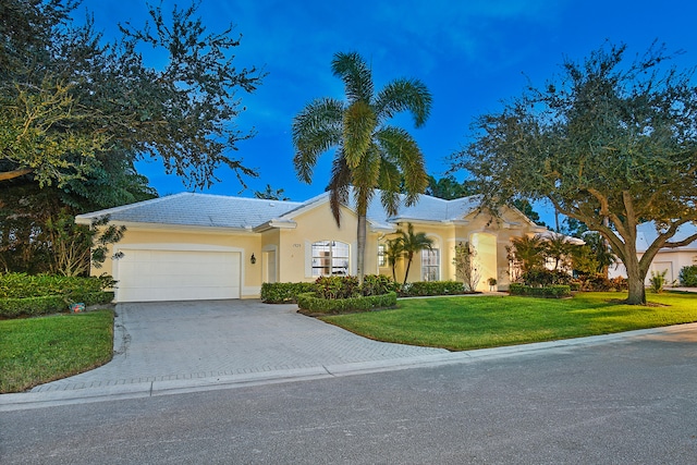 view of front of property featuring a tile roof, a front yard, stucco siding, decorative driveway, and an attached garage