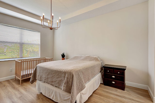 bedroom featuring a raised ceiling, light hardwood / wood-style flooring, and a chandelier