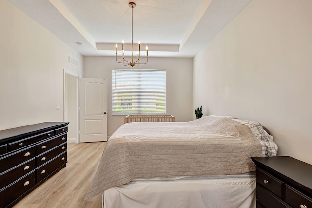 bedroom featuring a tray ceiling, light hardwood / wood-style floors, and an inviting chandelier