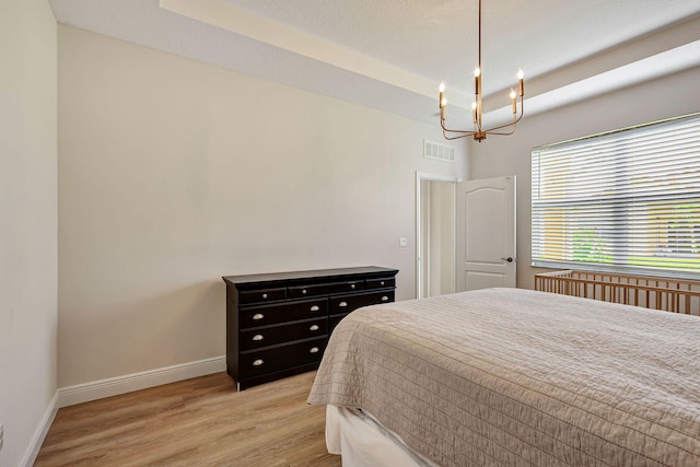 bedroom with a tray ceiling, a chandelier, and light hardwood / wood-style floors