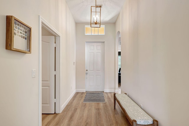 entryway featuring light wood-type flooring, a towering ceiling, a textured ceiling, and a chandelier