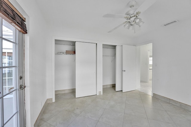 unfurnished bedroom with ceiling fan, light tile patterned floors, and two closets